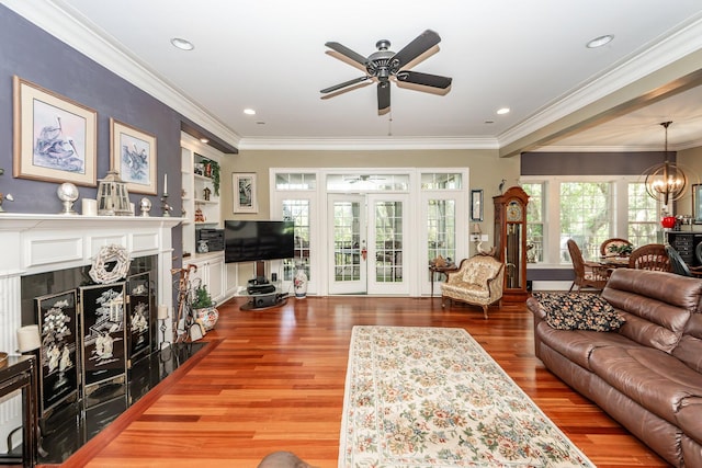 living room featuring crown molding, ceiling fan with notable chandelier, a tile fireplace, and wood finished floors