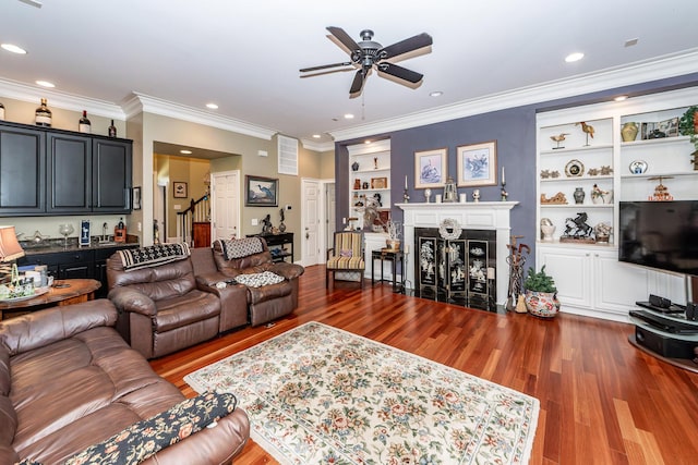 living room with stairs, wood finished floors, ceiling fan, built in shelves, and a fireplace with flush hearth