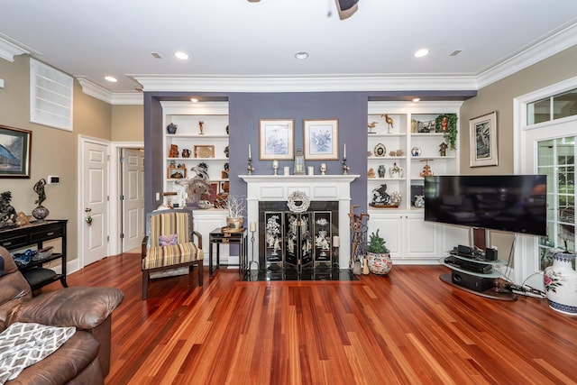 living room with ornamental molding, wood finished floors, ceiling fan, built in shelves, and a fireplace with flush hearth