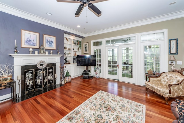living area with crown molding, ceiling fan, a fireplace with flush hearth, and wood finished floors