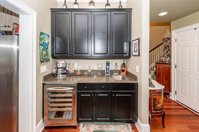 bar featuring freestanding refrigerator, wood finished floors, beverage cooler, a sink, and wet bar