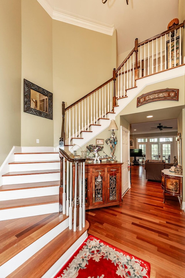 stairs with crown molding, a high ceiling, a ceiling fan, and wood finished floors