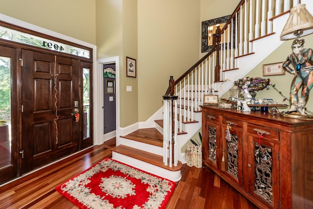 entryway featuring baseboards, a high ceiling, wood finished floors, and stairway