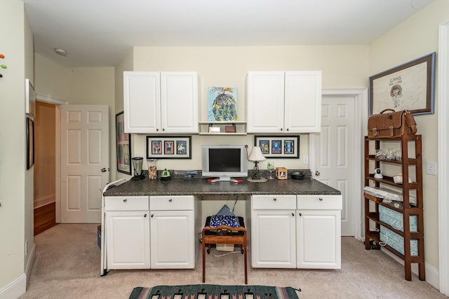 office with baseboards, built in desk, and light carpet