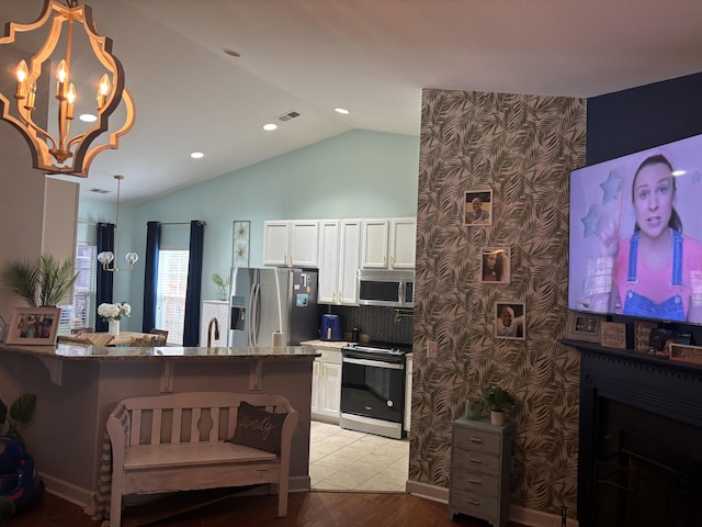 kitchen with stone counters, appliances with stainless steel finishes, white cabinets, decorative light fixtures, and vaulted ceiling