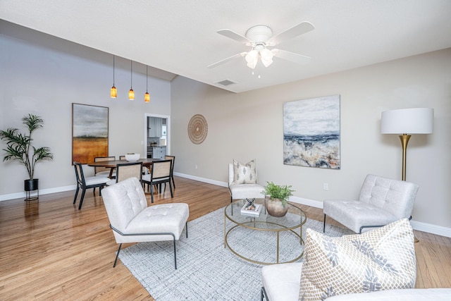 living room featuring light wood-type flooring, baseboards, visible vents, and ceiling fan