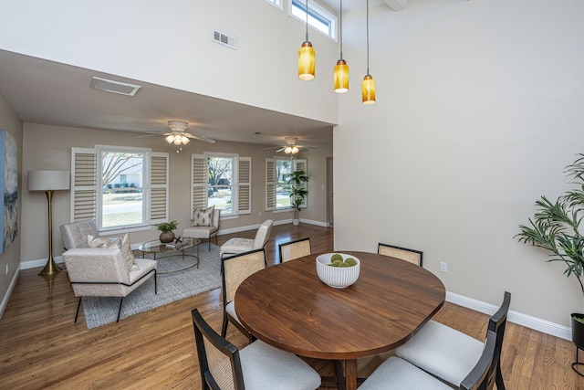 dining area featuring baseboards, visible vents, ceiling fan, a towering ceiling, and light wood-type flooring