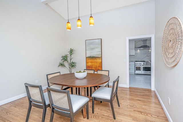 dining room featuring light wood-style flooring, baseboards, and a towering ceiling