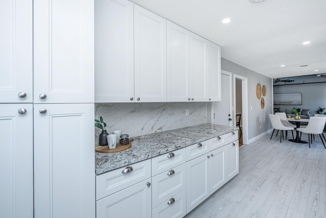 kitchen with light stone counters, light wood finished floors, recessed lighting, white cabinets, and backsplash