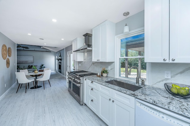 kitchen featuring wall chimney range hood, double oven range, dishwasher, light stone counters, and a sink