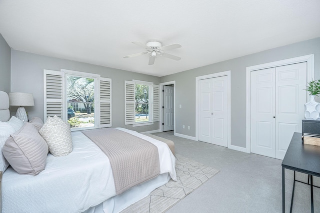 bedroom with ceiling fan, baseboards, two closets, and light carpet