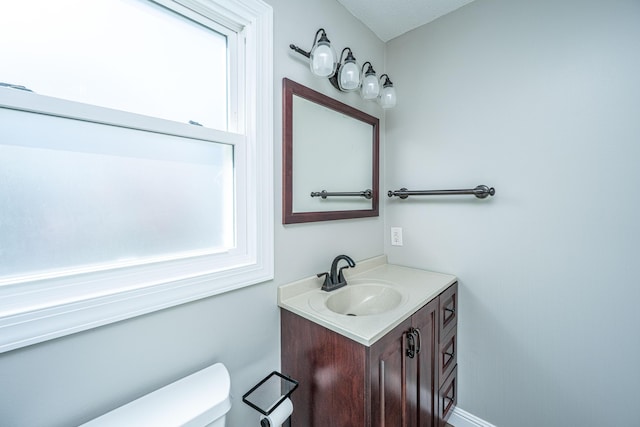 half bathroom featuring a healthy amount of sunlight, toilet, and vanity