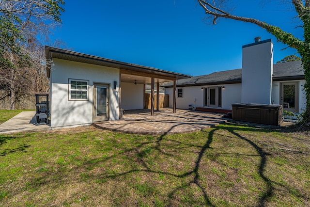 back of property with a lawn, a hot tub, and a patio area