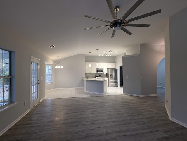 unfurnished living room with visible vents, vaulted ceiling, light wood-style flooring, and ceiling fan with notable chandelier