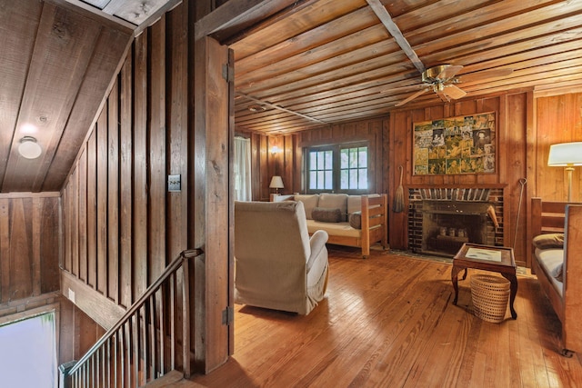 living area with ceiling fan, light hardwood / wood-style floors, a brick fireplace, wooden ceiling, and wood walls