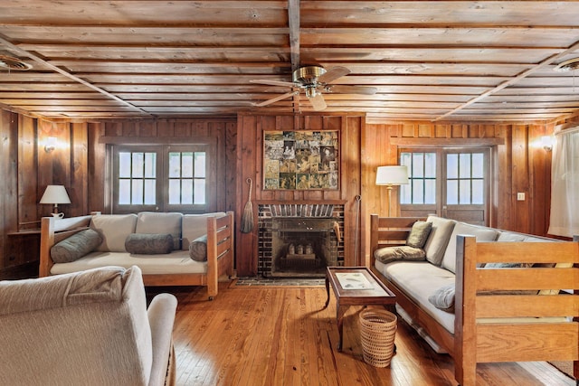 living room with a healthy amount of sunlight, wood walls, a fireplace, and light hardwood / wood-style flooring