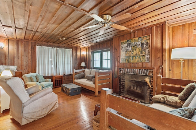 living room with wood ceiling, light hardwood / wood-style flooring, ceiling fan, wooden walls, and a brick fireplace