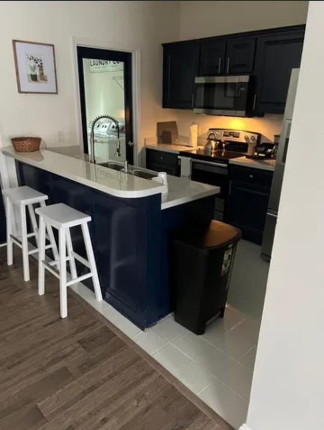 kitchen with light wood-type flooring, appliances with stainless steel finishes, sink, kitchen peninsula, and a breakfast bar