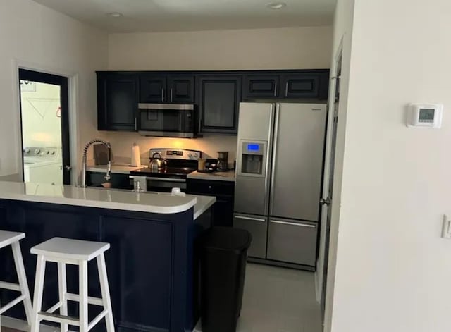 kitchen with sink, a breakfast bar area, appliances with stainless steel finishes, washing machine and clothes dryer, and kitchen peninsula