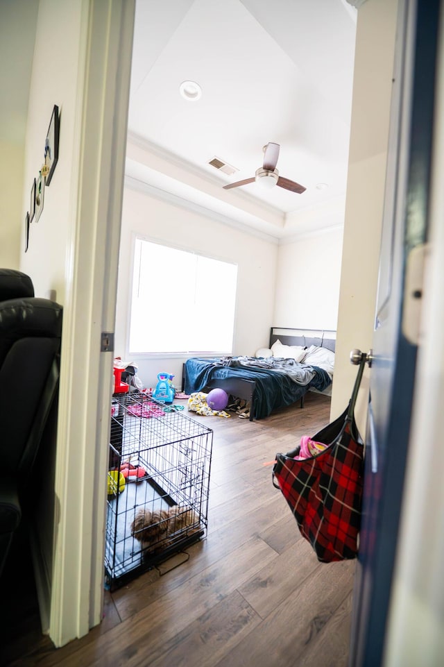 bedroom featuring a raised ceiling, crown molding, dark hardwood / wood-style floors, and ceiling fan