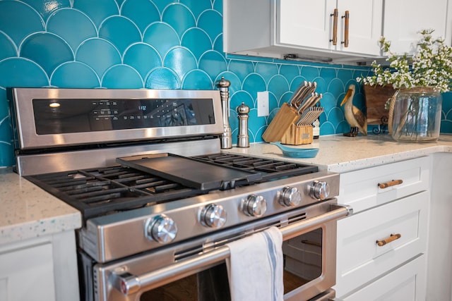 kitchen featuring white cabinets, light stone counters, decorative backsplash, and gas range