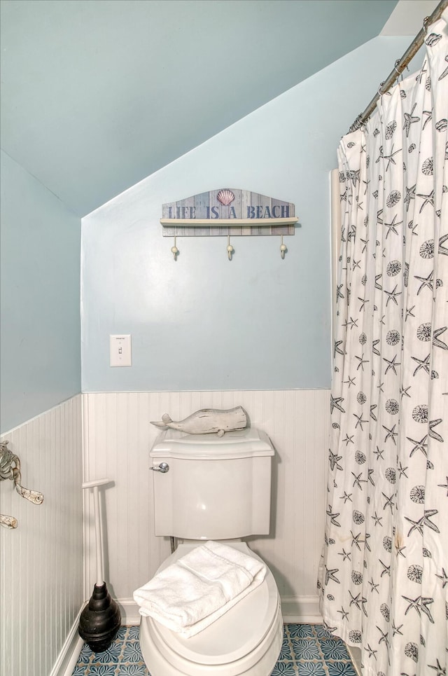 full bath featuring toilet, a shower with curtain, lofted ceiling, and a wainscoted wall