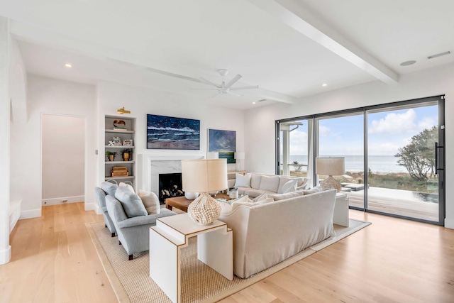 living room featuring beamed ceiling, light wood-type flooring, a water view, and a high end fireplace