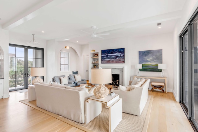 living room featuring beam ceiling, ceiling fan, french doors, light hardwood / wood-style floors, and a fireplace