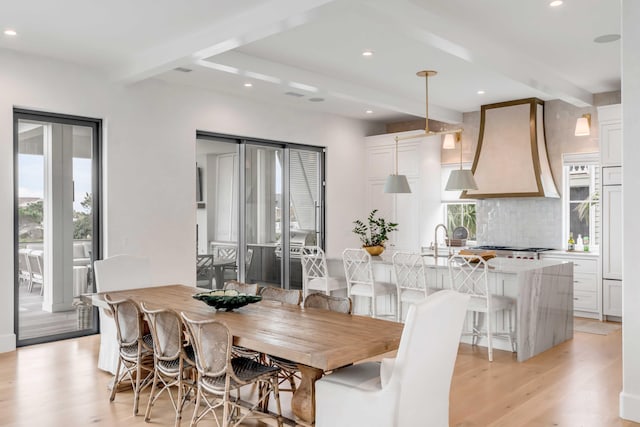 dining room with beamed ceiling, light wood-type flooring, and sink