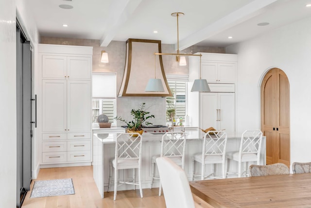 kitchen featuring pendant lighting, a breakfast bar, beam ceiling, and white cabinetry