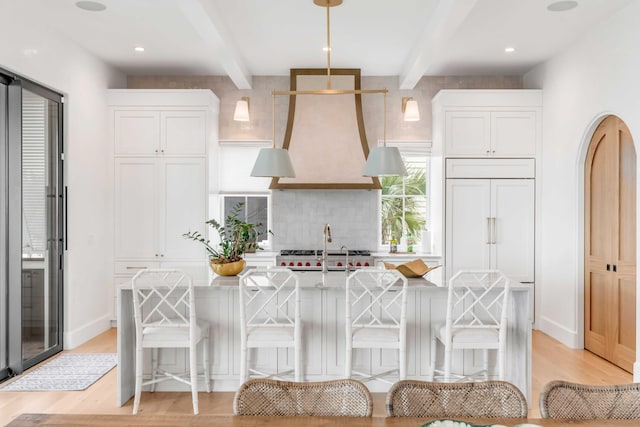 kitchen featuring beam ceiling, decorative light fixtures, light hardwood / wood-style flooring, white cabinets, and a breakfast bar area