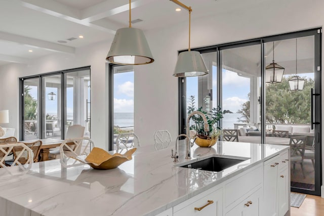 kitchen featuring white cabinets, a water view, sink, light stone countertops, and decorative light fixtures