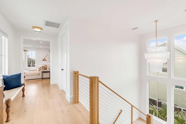 corridor featuring light wood-type flooring, a wealth of natural light, and a notable chandelier