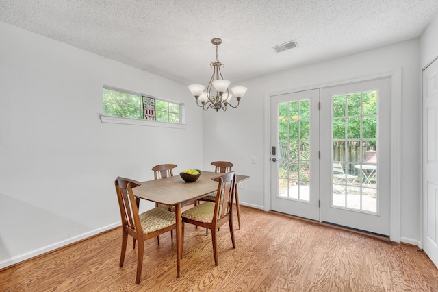 dining space featuring a textured ceiling, a notable chandelier, visible vents, and light wood-style floors