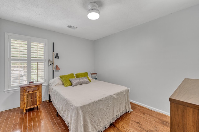 bedroom featuring visible vents, a textured ceiling, baseboards, and wood finished floors