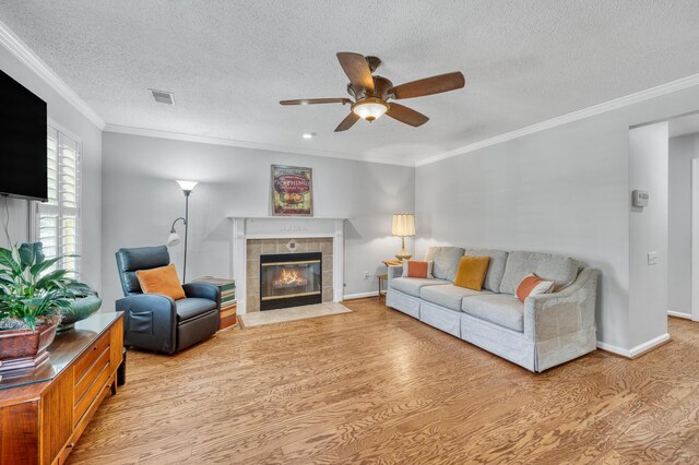 living area featuring a tiled fireplace, a ceiling fan, light wood finished floors, and a textured ceiling