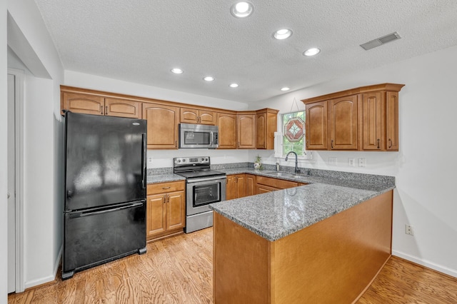 kitchen featuring brown cabinets, appliances with stainless steel finishes, a sink, a peninsula, and visible vents