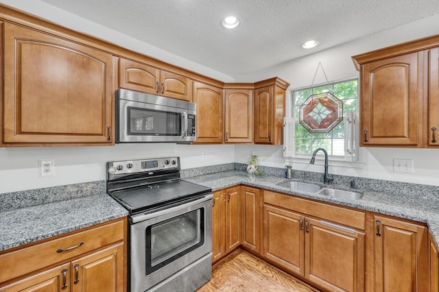 kitchen with a sink, stainless steel appliances, brown cabinets, and a textured ceiling