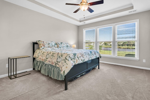 carpeted bedroom with a raised ceiling, ceiling fan, and crown molding