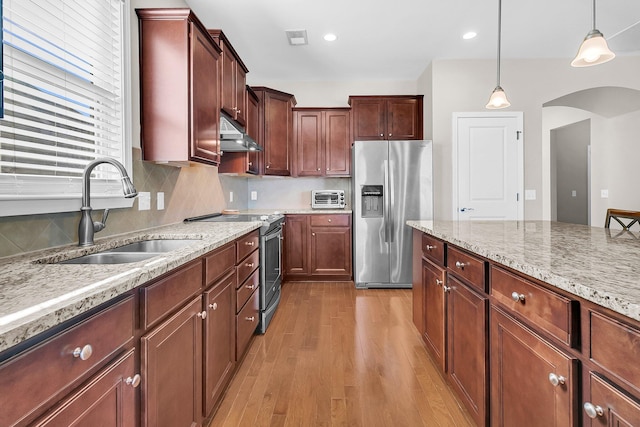 kitchen with pendant lighting, sink, light stone countertops, light wood-type flooring, and appliances with stainless steel finishes