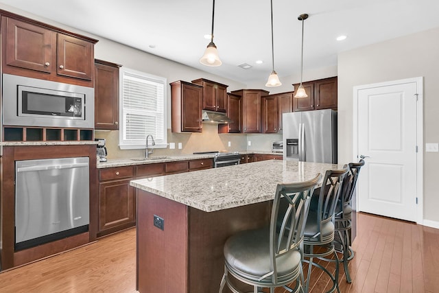 kitchen featuring a kitchen breakfast bar, stainless steel appliances, sink, a kitchen island, and hanging light fixtures