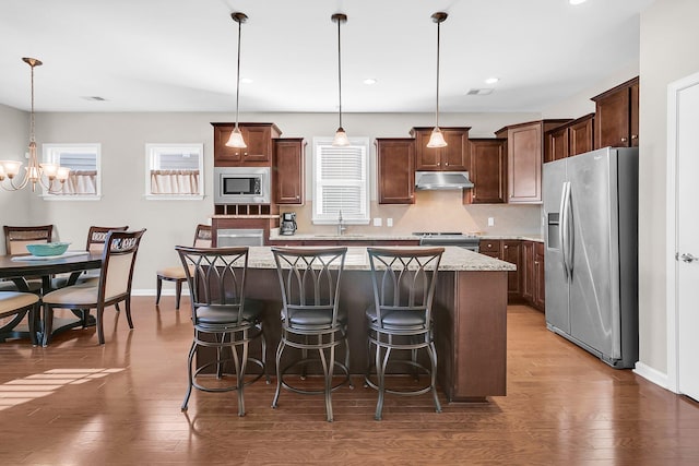 kitchen with dark wood-type flooring, hanging light fixtures, a kitchen island, and stainless steel appliances