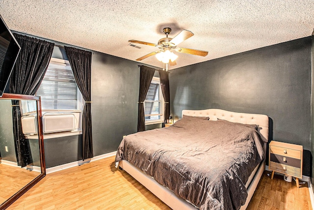 bedroom with cooling unit, ceiling fan, a textured ceiling, and light wood-type flooring