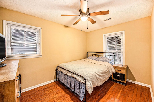 bedroom featuring multiple windows, ceiling fan, dark wood-type flooring, and a textured ceiling