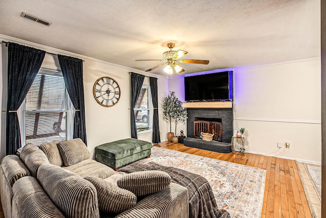 living room with a fireplace, wood-type flooring, ceiling fan, crown molding, and a textured ceiling