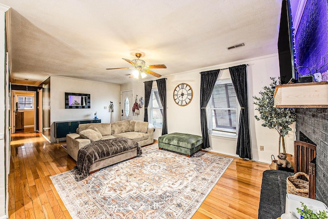 living room with ceiling fan, hardwood / wood-style floors, a textured ceiling, and a fireplace