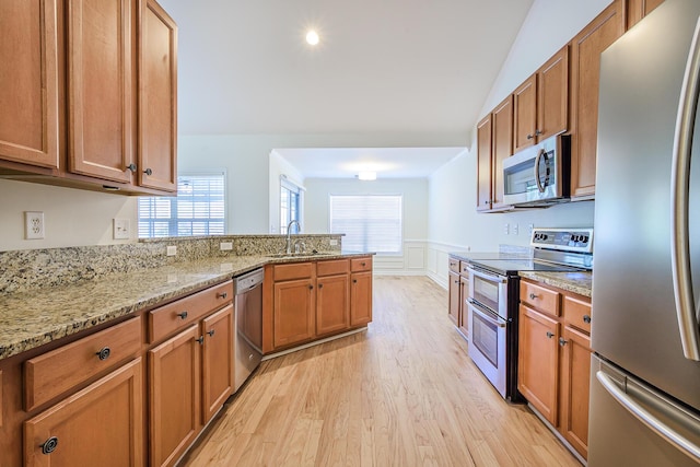 kitchen with light wood-type flooring, a sink, stainless steel appliances, a peninsula, and wainscoting