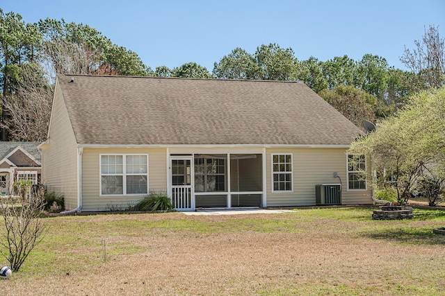 back of property with a shingled roof, central air condition unit, an outdoor fire pit, a lawn, and a sunroom