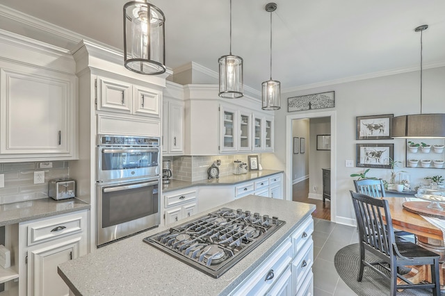 kitchen featuring decorative light fixtures, white cabinets, ornamental molding, stainless steel appliances, and light stone countertops