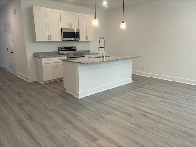 kitchen with a sink, appliances with stainless steel finishes, wood finished floors, white cabinets, and a kitchen island with sink